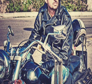 A man in a leather jacket sitting on a motorcycle.